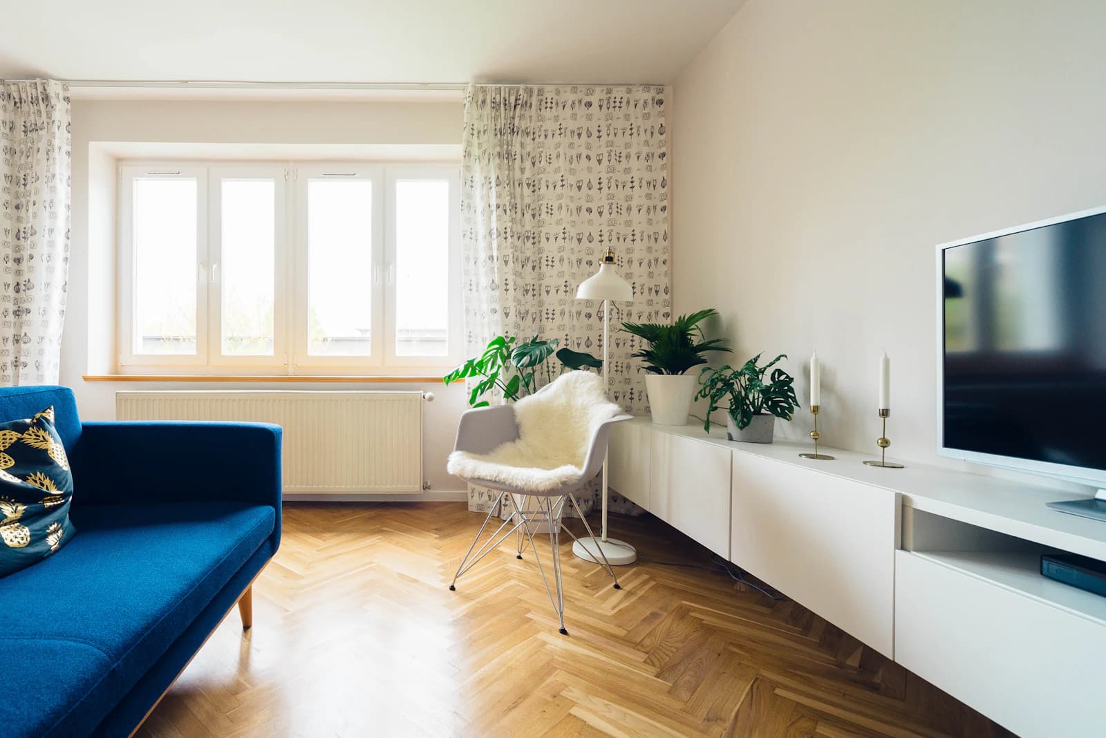 A sunny loft with a blue velvet sofa, herringbone floor and low white cabinets