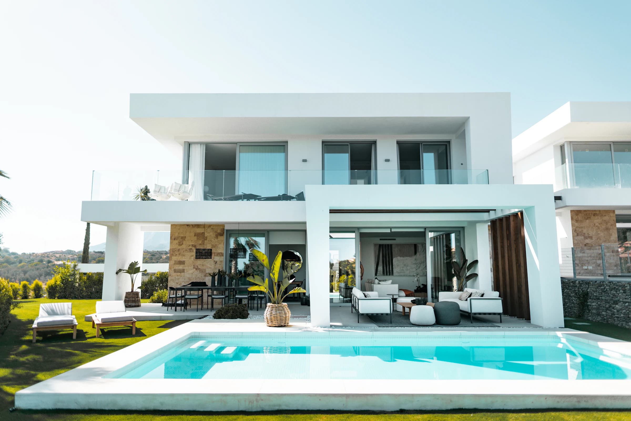 A white two-storey modern villa with a covered terrace and a pool, under a clear sky