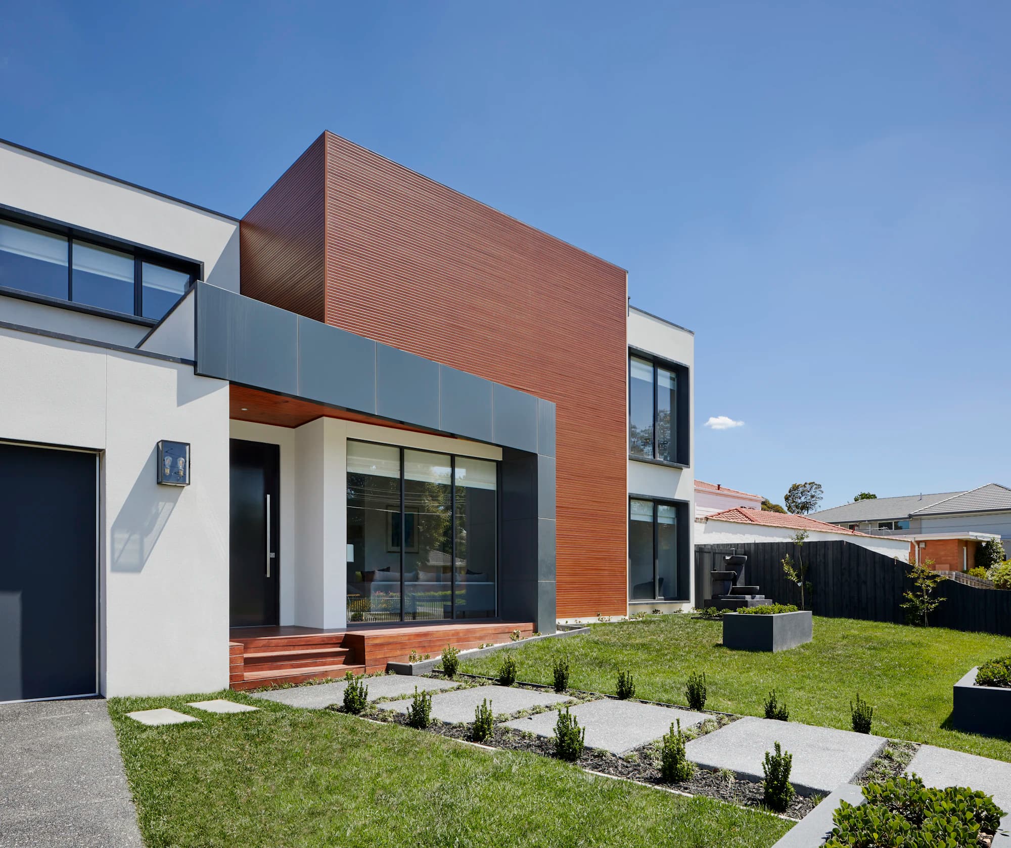 A townhouse facade of white render, grey panels and warm cedar cladding