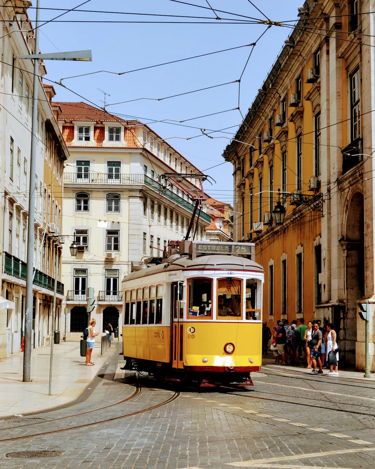 A yellow tram on a cobbled Lisbon street between pastel facades