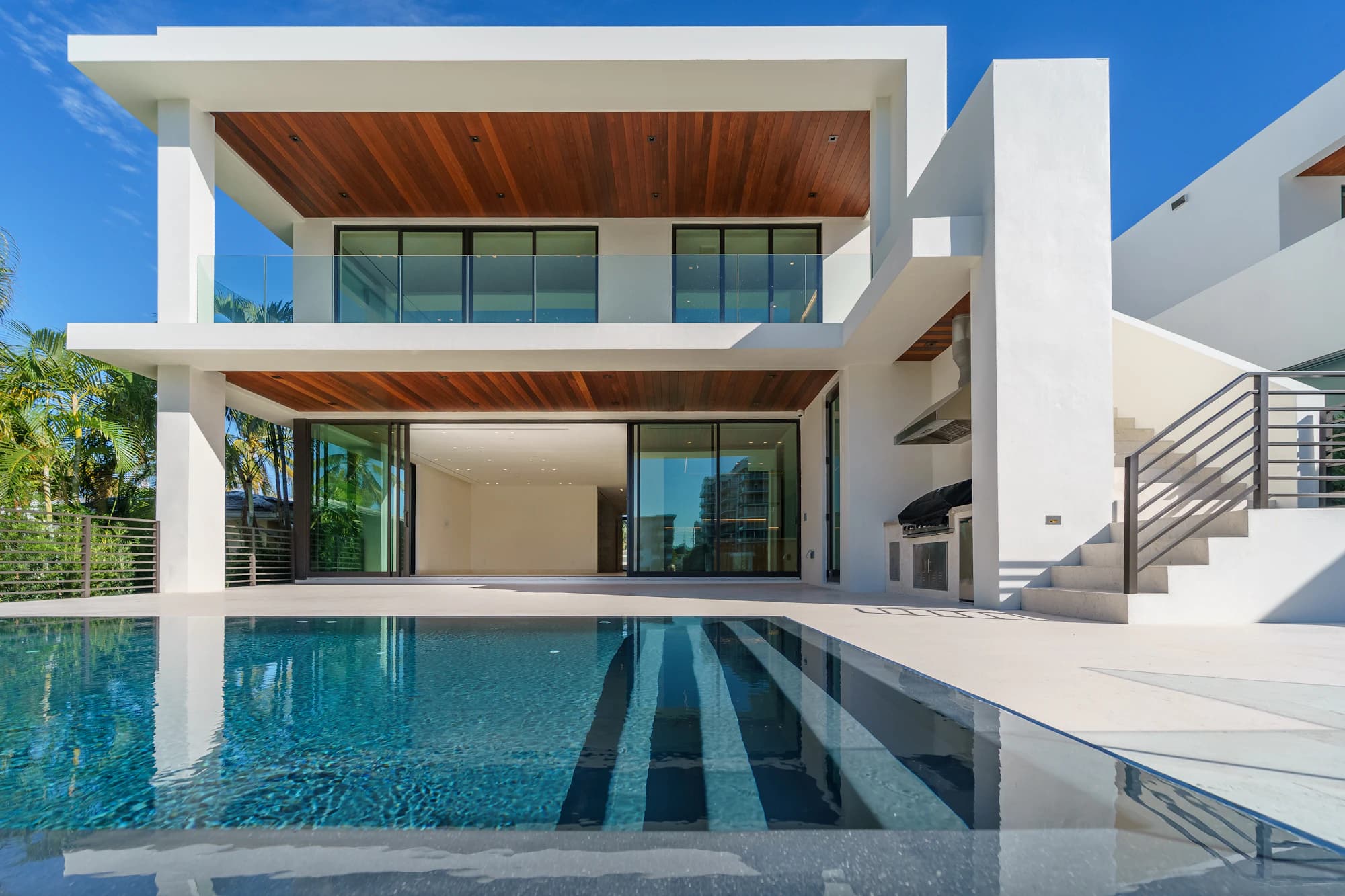 A white villa with a timber soffit and floor-to-ceiling glass facing a long pool