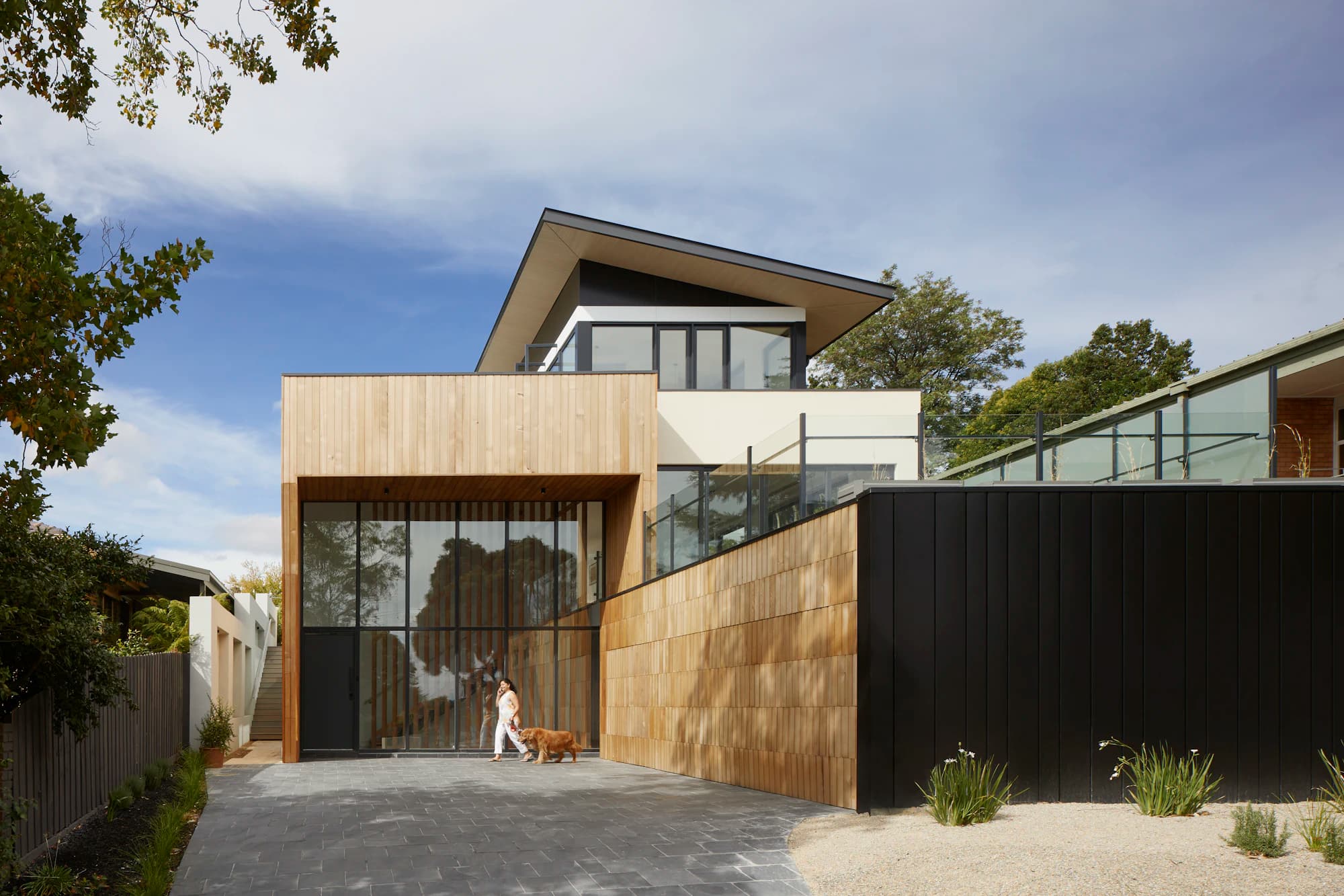 A two-storey house clad in pale timber and black panels on a quiet street