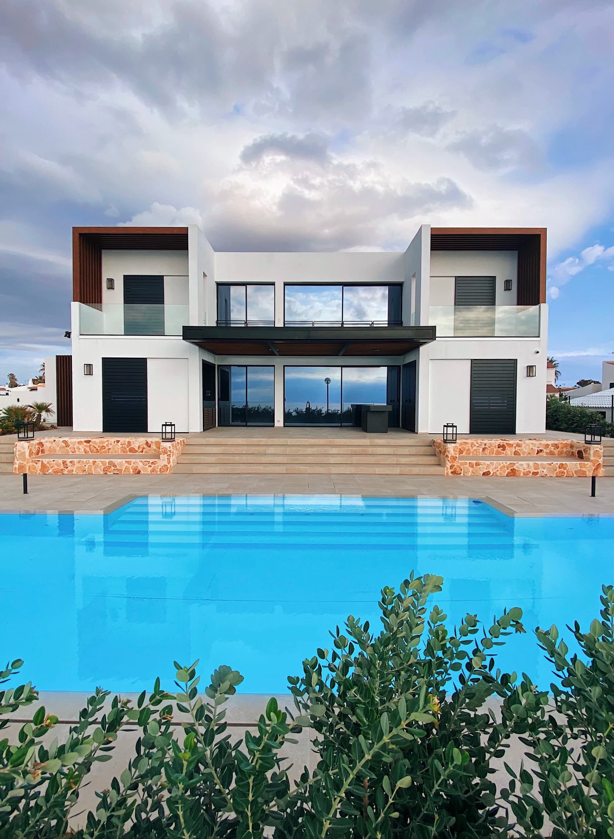 A symmetrical white villa with glass balconies above a wide pool